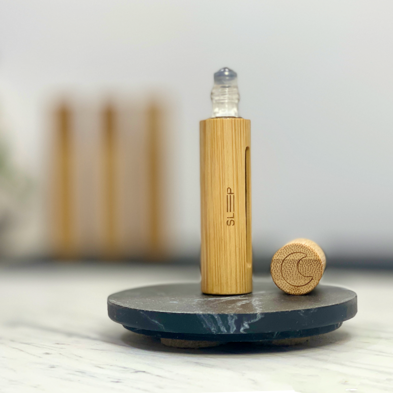 Essential oil roller, Sleep Blend, in a sleek bamboo case with a cap opened to show the ball roller.